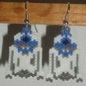 Peut inclure: Boucles d'oreilles perlées faites à la main avec un motif géométrique en blanc, bleu et gris. Les boucles d'oreilles ont une forme rectangulaire avec un accent bleu central et des crochets d'oreilles argentés. Le travail de perles complexe crée un aspect texturé.