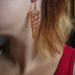 Op de afbeelding: Een paar oorbellen met een roze en wit schelpdesign met gouden accenten. De schelpen zijn geperst en hangen aan gouden haakjes.