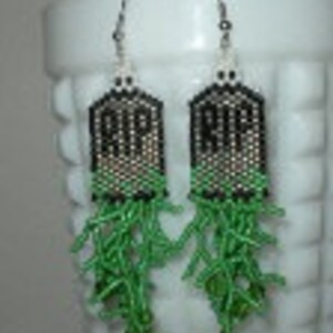 Puede incluir: Un par de pendientes de cuentas negras y verdes con un diseño 'RIP' y cuentas verdes colgantes.