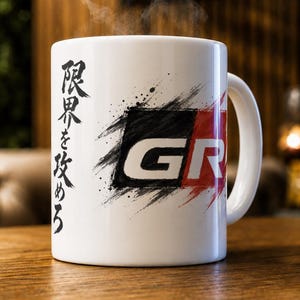 Puede incluir: Una taza de cerámica blanca con un logotipo GR en negro y rojo con efecto de pincelada. El lateral de la taza muestra texto japonés vertical en tinta negra. El vapor sale de la parte superior de la taza, indicando una bebida caliente.