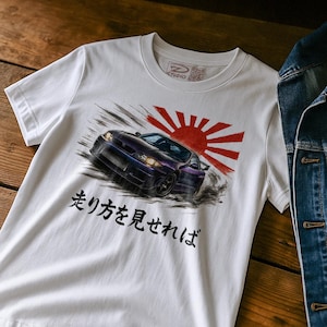 Könnte beinhalten: Weißes T-Shirt mit einem lila Sportwagen-Motiv, einer roten Sonne und japanischem Text. Das Auto wird in Bewegung mit Rauch und Geschwindigkeitslinien dargestellt. Das T-Shirt hat einen Rundhalsausschnitt und kurze Ärmel.
