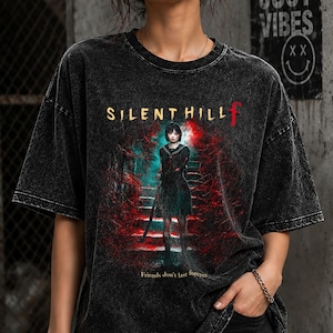 May include: A black acid-wash t-shirt featuring a graphic print of a character standing on stairs with the text SILENT HILL f and the phrase Friends don't last forever. The shirt has a crew neckline and short sleeves with a distressed, faded appearance.
