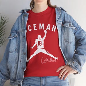 May include: Red t-shirt with the word "ICEMAN" in white block letters above a white silhouette of a football player in mid-air, holding a football. The player's jersey number is "18". A signature is below the player.
