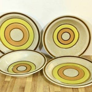 Puede incluir: Juego de cuatro cuencos de cerámica con un borde marrón y círculos concéntricos de amarillo, naranja y marrón sobre un fondo beige.