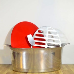 May include: A silver oval-shaped pot with a red lid and a silver grill insert.