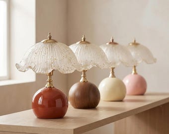Könnte beinhalten: Vier Tischlampen mit geriffelten, klaren Glasschirmen mit Goldsprenkeln und messingfarbenen Elementen. Die Sockel sind kugelförmig und in vier verschiedenen Ausführungen erhältlich: glänzend terrakotta, natürliches Holz, cremeweiß und zartrosa.