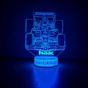 May include: A blue LED night light shaped like a Formula 1 race car. The name "Isaac" is illuminated at the base of the car. The light has a detailed outline of the car's components, including the wheels and spoiler.