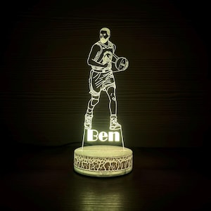 May include: A glowing LED basketball player lamp. The lamp features a basketball player holding a ball, with the name "Ben" illuminated at the base. The lamp has a round base with a decorative pattern and is lit with a soft, warm light.