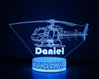 May include: A blue LED night light featuring a helicopter design with the name "Daniel" in white. The light has a cracked pattern base and a triangular top with the helicopter outline.
