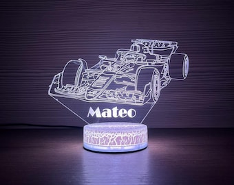 May include: A Formula 1 race car night light with the name "Mateo" etched into the acrylic. The base of the light has a cracked pattern and emits a soft glow. The car is white and the base is a light blue.