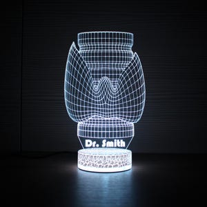 May include: A white, 3D-printed lamp with a medical-themed design, featuring a grid-like structure and the text "Dr. Smith" on the base. The lamp emits a soft, glowing light, creating a modern and unique aesthetic.
