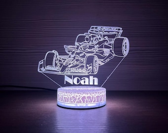 May include: A Formula 1 race car illuminated night light with the name "Noah" displayed. The light has a white outline of the car and a patterned base that glows with a purple hue. The background is dark.