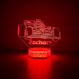 May include: A red illuminated Formula 1 race car night light with the name "Zachary" etched into the base. The light has a cracked, textured base and a detailed outline of the car.
