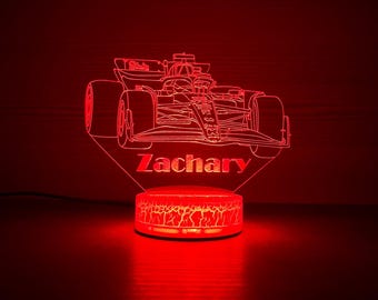 May include: A red illuminated Formula 1 race car night light with the name "Zachary" etched into the base. The light has a cracked, textured base and a detailed outline of the car.