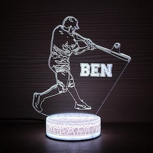 May include: An illuminated baseball-themed night light. The design features a batter mid-swing, with the name "BEN" displayed. The round base has a decorative pattern and emits a soft glow, suitable for a sports enthusiast's room.