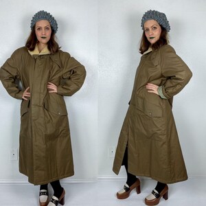 May include: A long brown coat with a faux fur collar and a zipper closure. The coat has a belt and two pockets. The model is wearing a gray knitted hat.