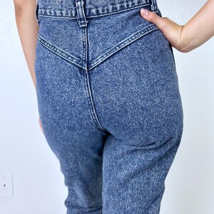 May include: Acid wash denim jeans with a high waist and a unique V-shaped yoke detail. The jeans have a classic five-pocket design and a straight leg. The denim is a medium blue wash with a slightly faded appearance, giving them a vintage look.