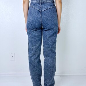 May include: Acid wash denim jeans with a high waist and tapered leg. The jeans have a classic five-pocket design and are cuffed at the ankles. The model is wearing a black and white striped top.