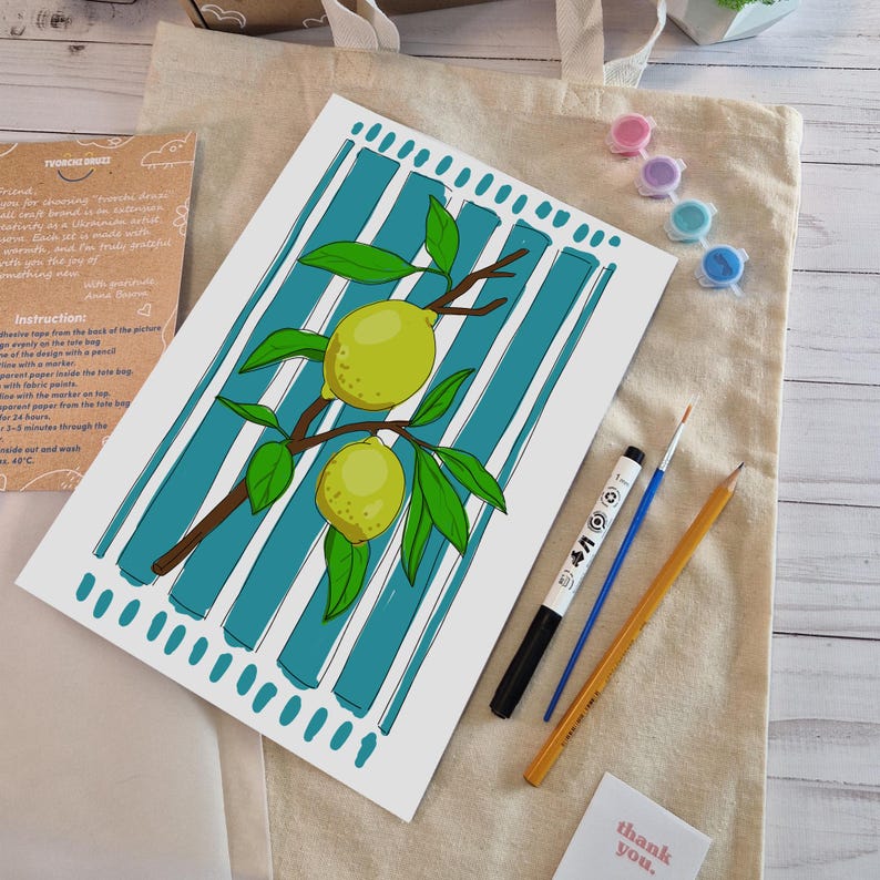 May include: A white rectangular paper print featuring a brown branch with two yellow lemons and green leaves, set against a background of vertical teal stripes. The print is accompanied by a black marker, a blue paintbrush, and a yellow pencil.