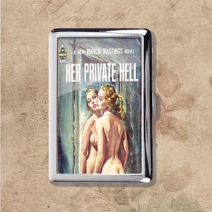 May include: A silver cigarette case featuring a vintage book cover design. The cover art depicts two nude women, with the title "HER PRIVATE HELL" in bold white letters. The case has a shiny, reflective surface.