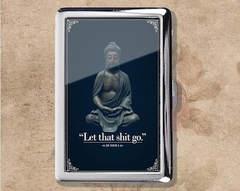 Puede incluir: Un pitillera plateada con un fondo azul oscuro que presenta una estatua de Buda sentado. La pitillera tiene detalles decorativos en las esquinas y la cita "Let that shit go." atribuida a Buda.