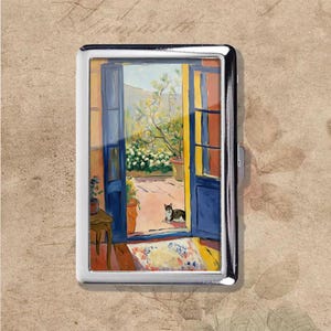 Puede incluir: Un pitillera plateada con una pintura de un patio soleado. La obra de arte representa puertas azules, plantas en macetas y un gato. La pintura tiene un estilo impresionista, con un enfoque en la luz y la sombra.