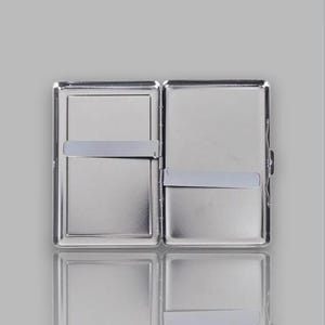 May include: Open, silver-colored cigarette case with a rectangular shape. The case is divided into two compartments, each with a silver band to hold items in place. The case is open, revealing the interior, and has a reflective surface.