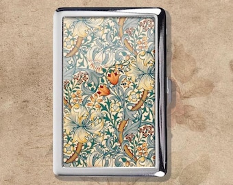 Pode incluir: Um porta-cigarros prateado retangular com um padrão floral. O design apresenta lírios creme, detalhes laranja e folhas verdes sobre um fundo creme. O porta-cigarros tem um acabamento metálico brilhante e um fecho.