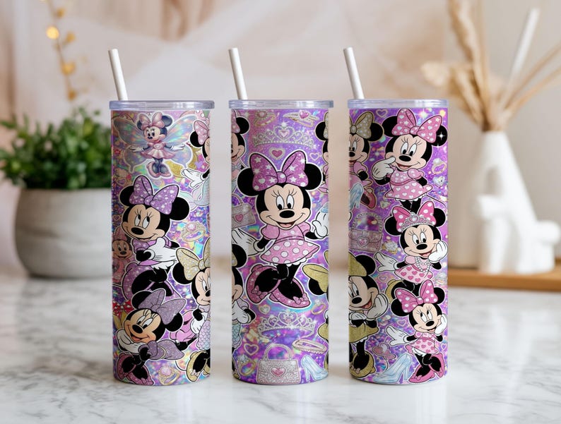 Op de afbeelding: Drie cilindrische bekers met doorzichtige deksels en witte rietjes, voorzien van een herhalend patroon van Minnie Mouse in diverse houdingen, gekleed in roze jurken met stippen en strikken, tegen een levendige paarse achtergrond met glitters.