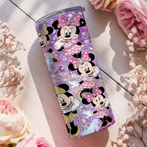 Op de afbeelding: Een cilindrische roestvrijstalen beker met een levendige paarse achtergrond en een herhalend patroon van Minnie Mouse in verschillende houdingen, gekleed in roze jurken met stippen en strikken, geaccentueerd met glitters en kleine hartjes.