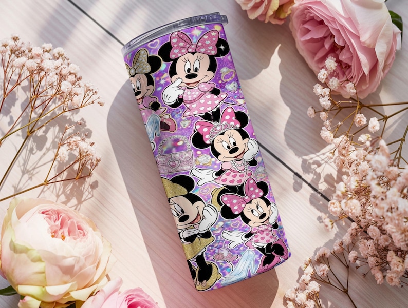Op de afbeelding: Een cilindrische roestvrijstalen beker met een levendige paarse achtergrond en een herhalend patroon van Minnie Mouse in verschillende houdingen, gekleed in roze jurken met stippen en strikken, geaccentueerd met glitters en kleine hartjes.