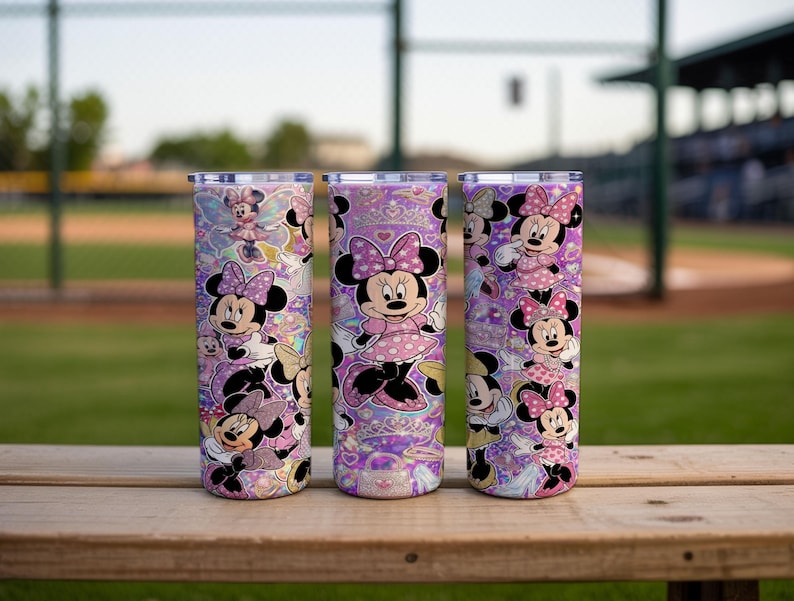 Op de afbeelding: Drie cilindrische bekers met een herhalend patroon van Minnie Mouse in verschillende houdingen, gekleed in roze jurken met stippen en strikken. De achtergrond van de bekers is levendig paars met holografische glitters, hartjes en kronen.