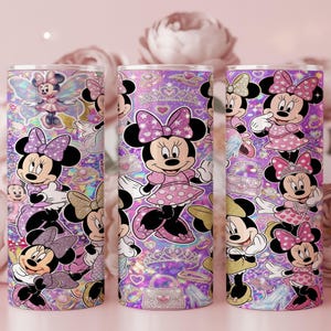Op de afbeelding: Drie cilindrische bekers met een herhalend patroon van Minnie Mouse in verschillende houdingen, gekleed in roze en paarse jurken met stippen en strikken. De achtergrond is een levendig paars en roze holografisch ontwerp met kronen, tasjes en hartjes.