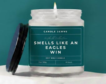 Può includere: Una candela accesa in cera di soia in un barattolo di vetro trasparente con un'etichetta verde acqua. L'etichetta recita "Smells Like An Eagles Win" dalla "Football Collection". Il barattolo è da 226g e ha un tempo di combustione di 40 ore.