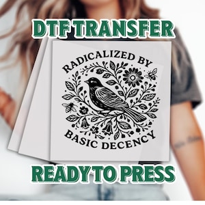 May include: A white DTF transfer sheet with a black illustration of a bird surrounded by flowers, leaves, and bees. The text "RADICALIZED BY BASIC DECENCY" and "READY TO PRESS" are also included.