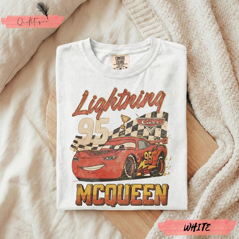May include: White t-shirt featuring a graphic of Lightning McQueen from the Cars movie. The design includes the text "Lightning 95 McQueen" in a vintage style, with a checkered flag and a trophy.