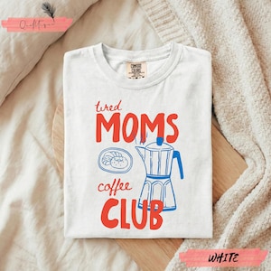 May include: White t-shirt with the words "tired MOMS coffee CLUB" in red and blue. The design includes a coffee pot and a pastry. The shirt is made of Comfort Colors material.