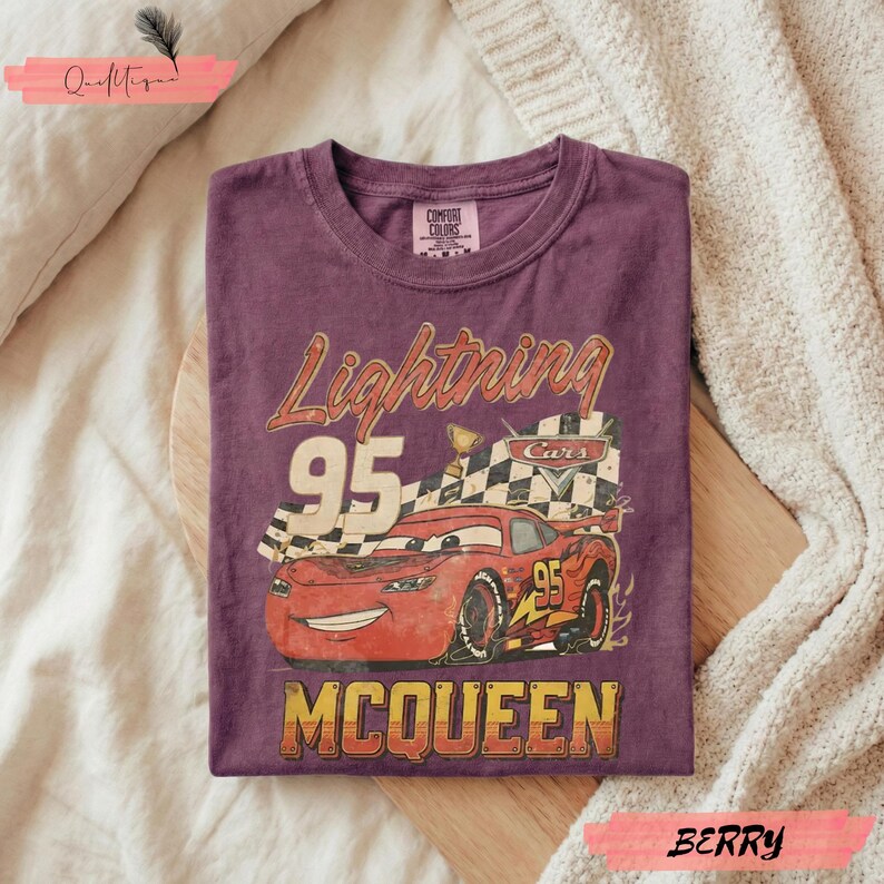 May include: Berry-colored t-shirt featuring a graphic of Lightning McQueen from the movie Cars. The design includes the text "Lightning 95 McQueen" with a checkered flag and a smiling red race car.