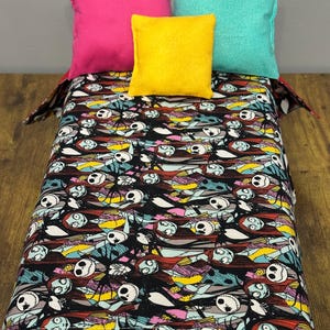 Peut inclure: Un lit miniature avec une couverture noire &agrave; motifs repr&eacute;sentant des personnages de L'&Eacute;trange No&euml;l de Monsieur Jack. Le lit est orn&eacute; de quatre oreillers carr&eacute;s roses, jaunes, turquoise et blancs.