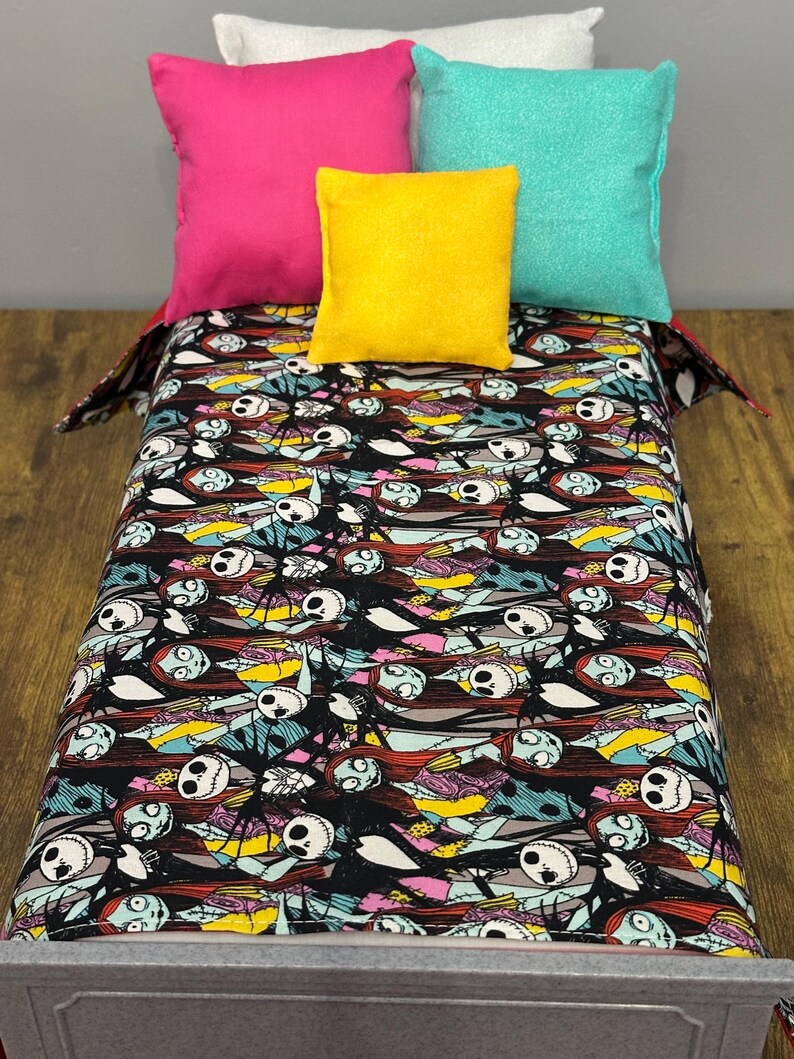 Peut inclure: Un lit miniature avec une couverture noire &agrave; motifs repr&eacute;sentant des personnages de L'&Eacute;trange No&euml;l de Monsieur Jack. Le lit est orn&eacute; de quatre oreillers carr&eacute;s roses, jaunes, turquoise et blancs.