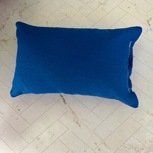 K&ouml;nnte beinhalten: Ein rechteckiges, einfarbig blaues Kissen. Das Kissen hat einen leuchtenden Blauton und scheint aus einem weichen Stoff zu bestehen. Das Kissen liegt auf einer hellen, gemusterten Oberfl&auml;che.