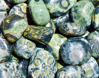 May include: Close-up of a collection of polished stones in shades of green, black, and gray. The stones have a smooth, rounded shape and varying patterns, creating a natural and textured appearance. Ideal for jewelry making or collecting.