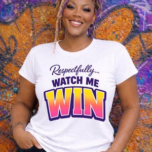 May include: White t-shirt with the text "Respectfully... WATCH ME WIN" in a purple, yellow, and pink design. The shirt is worn by a person with locs and hoop earrings, posing in front of a colorful graffiti wall.