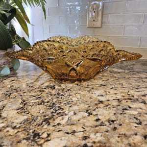 Puede incluir: Cuenco de vidrio color ámbar con un diseño de estrella y diamante. El cuenco tiene un borde festoneado y una forma acampanada, similar a un ala. El vidrio tiene una superficie texturizada, y el cuenco está sobre una encimera de granito.