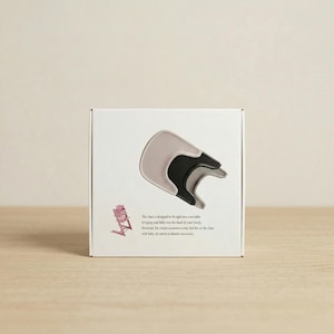 May include: A white box with a product image of a light gray and black baby chair attachment. The box also features a small pink illustration of a baby chair and text describing the product's features.