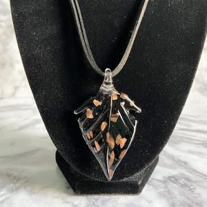 May include: A black leather cord necklace with a black and gold glass leaf pendant.