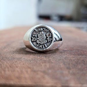 May include: A white ceramic mug with a black handle and the text "But First, Coffee" in a bold, black font. The mug is set against a blurred background, suggesting a cozy setting.