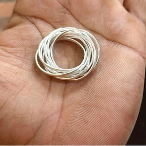 Può includere: Una collezione di anelli d'argento, disposti in modo circolare. Gli anelli sono sottili e sembrano essere fatti di metallo lucido. Gli anelli sono tenuti in una mano, con il tono della pelle della mano di colore marrone chiaro.