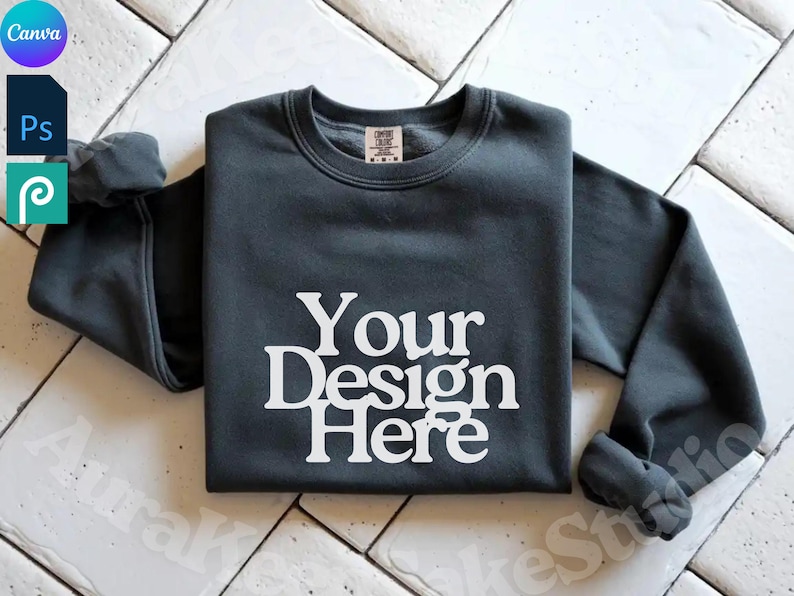 Pode incluir: Camisola cinza escuro com o texto "Your Design Here" em branco. A camisola de gola redonda de manga comprida &eacute; exibida em uma superf&iacute;cie de azulejos brancos. A camisa tem uma etiqueta na parte de tr&aacute;s do pesco&ccedil;o.