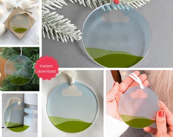 May include: Clear, round Christmas ornament with a landscape design. The ornament features a blue sky with a white cloud and green hills at the bottom. A white ribbon is attached for hanging. The words "Instant download" are on a red sticker.